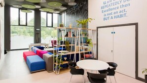 A modern office space with a colorful sofa, a white table with chairs, and a bookshelf with plants.