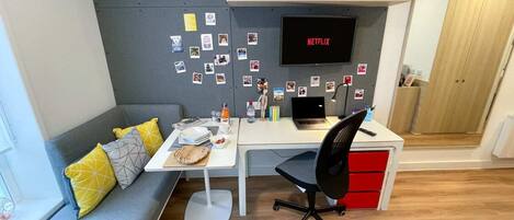 A modern office space with a desk, chair, and a couch. There is a shelf with binders and a television mounted on the wall.
