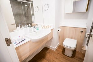 A modern bathroom with a white sink, toilet, and wooden flooring.