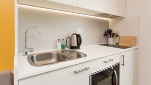 A modern kitchen with a stainless steel sink, a kettle, and a coffee machine. There are cabinets and a countertop with various kitchen utensils.