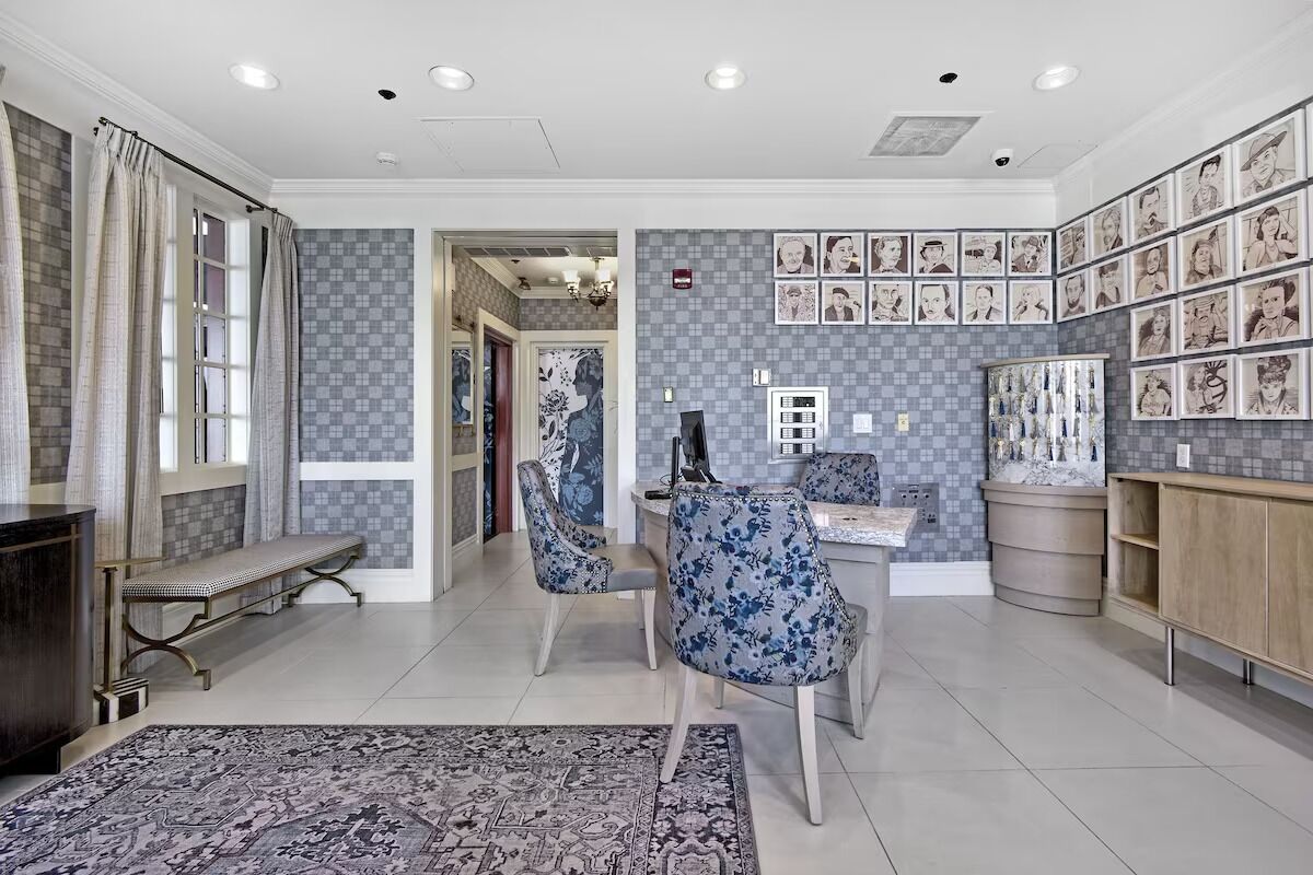 A spacious living room with a large rug, two blue floral armchairs, a bench, and a coffee table.