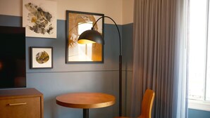 A hotel room with a round wooden table, a single orange chair, a black floor lamp, and artwork on the walls. - Luxurious Escape with Modern Touches in Heart of SF (San Francisco)