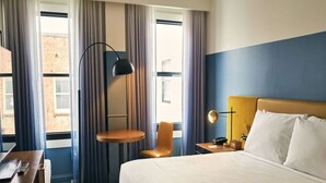 A hotel room with a large bed, a desk, a chair, a lamp, and a view of the outside through the window. - Sleek Boutique Room in Nob Hill Near Wharf, Shops & Grace Cathedral (San Francisco)