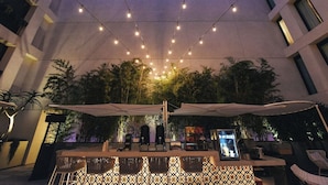 An outdoor dining area with string lights, umbrellas, and a view of trees and a building in the background. - Hollywood Room with Rooftop Pool, Outdoor Pool & Pets Allowed (Los Angeles)