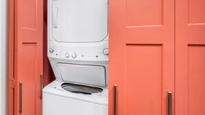 A compact laundry room with a front-loading washer and dryer, enclosed by red cabinets with silver handles. - Uptown Peach ~Best 4 Baylor games/visits ~Sleeps 5 (Waco)