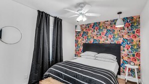 A bedroom with a bed, a ceiling fan, a small table, and a wall with a floral pattern. - Uptown Peach ~Best 4 Baylor games/visits ~Sleeps 5 (Waco)