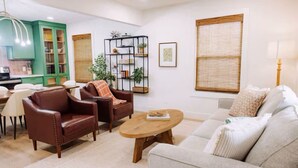 A living room with a sofa, two armchairs, a coffee table, and a dining area with a table and chairs. There is a kitchen in the background with green cabinets and a hanging light fixture. - Uptown Peach ~Best 4 Baylor games/visits ~Sleeps 5 (Waco)
