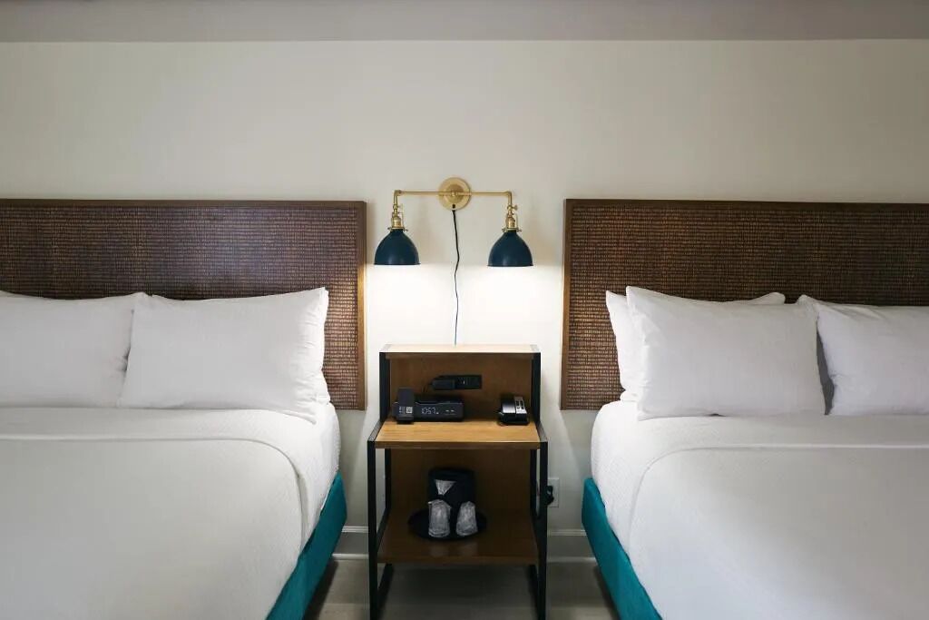 A hotel room with two beds, a nightstand with a lamp, and a small table with a radio.