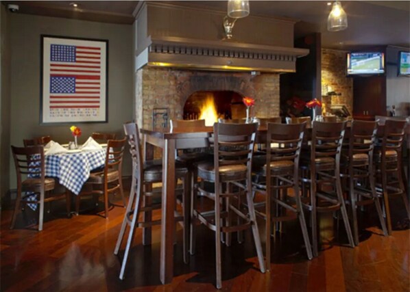 Un restaurante con chimenea de ladrillo, sillas de madera y una mesa con mantel a cuadros azules y blancos.