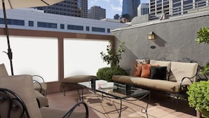 Una terraza en la azotea con una mesa de vidrio, sofá color beige y sillas exteriores.