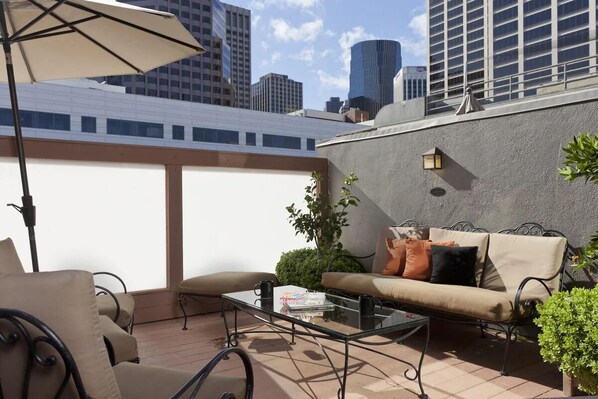 A rooftop patio with a glass table, beige sofa, and outdoor chairs.