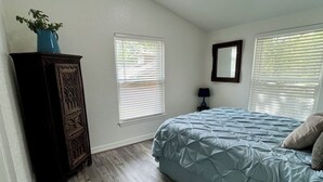 A bedroom with a bed, a dresser, a mirror, and two windows with blinds.