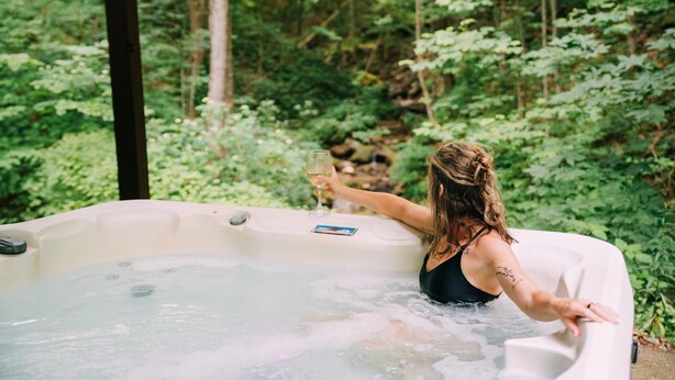 Una persona en un jacuzzi rodeada de abundante vegetación.