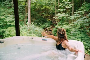 A person in a hot tub surrounded by lush greenery. - Creekside Oasis! A 3-bedroom cabin with a fantastic view in Birch Hollow. (Stanton)