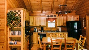 Interior de una cabaña de madera con cocina, comedor y estanterías.