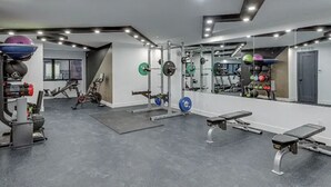 Un gimnasio moderno con equipamiento para levantar pesas, bicicletas estáticas y un espejo grande.
