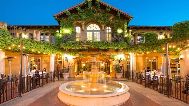 Une cour intérieure avec une fontaine centrale, entourée d’espaces de repos en plein air et d’un bâtiment doté d’un balcon.