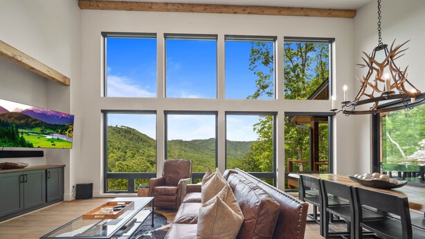 A spacious living room with a large window overlooking a scenic landscape, a leather sofa, a glass coffee table, and a wooden dining table. - Sky's the Limit - community pool, gym, hiking trails! (Boone)
