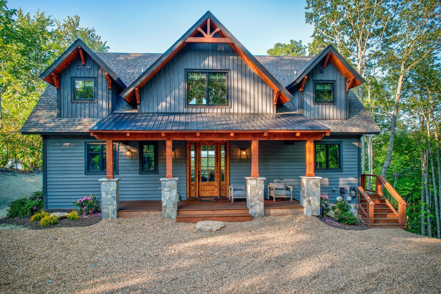 A large, two-story cabin with a prominent front porch, stone pillars, and a steeply pitched roof.