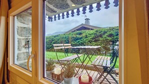 A window view of a patio with wooden furniture and potted plants.