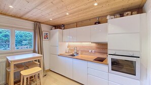 A compact kitchen with white cabinets, a wooden countertop, a sink, and an oven. There is a window with a view of greenery outside.