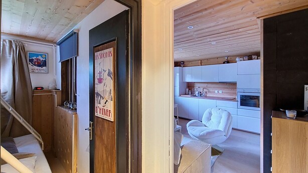 A modern interior with a wooden staircase, a kitchen area with white cabinets, and a white chair.