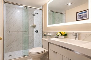 Un bany modern amb dutxa de vidre, un vàter, un lavabo amb mirall i una fotografia encadrada a la paret.