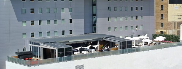 Un bâtiment moderne doté d’un toit plat, de nombreuses fenêtres et d’un espace extérieur abrité avec des parasols, aménagé pour accueillir des clients.