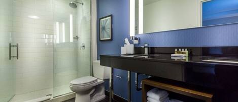 A modern bathroom with a glass-enclosed shower, a toilet, a black vanity with a mirror, and a blue accent wall.