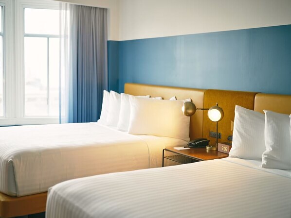 Una habitación de hotel con dos camas, una mesita de noche con lámpara y una ventana con cortinas.
