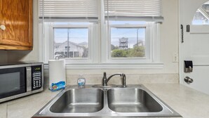 A kitchen with a double stainless steel sink, a microwave, and a window with blinds.