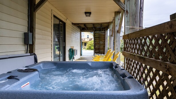 A hot tub on a covered porch with wooden railings and a view of the street.