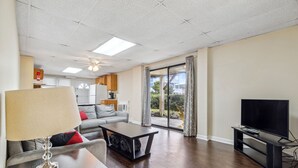 A modern living room with a sofa, coffee table, TV, and a view of the outdoors through large windows.