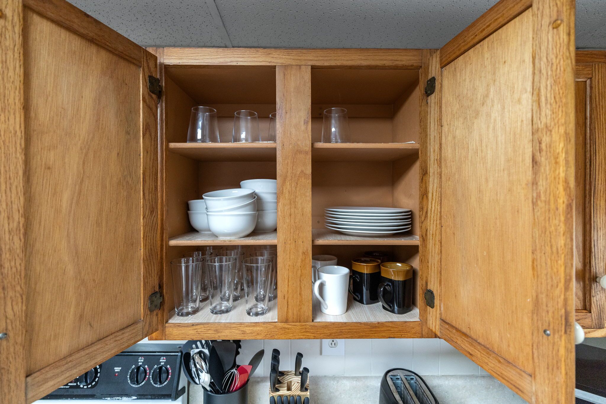 A wooden cabinet with shelves containing white bowls, plates, glasses, and mugs.