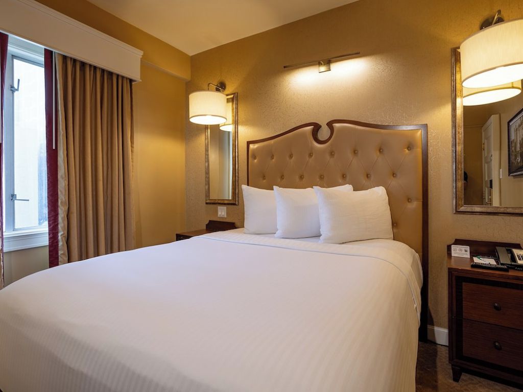 Ein Hotelzimmer mit einem großen Bett, einem Nachttisch, einer Lampe und einem Spiegel.