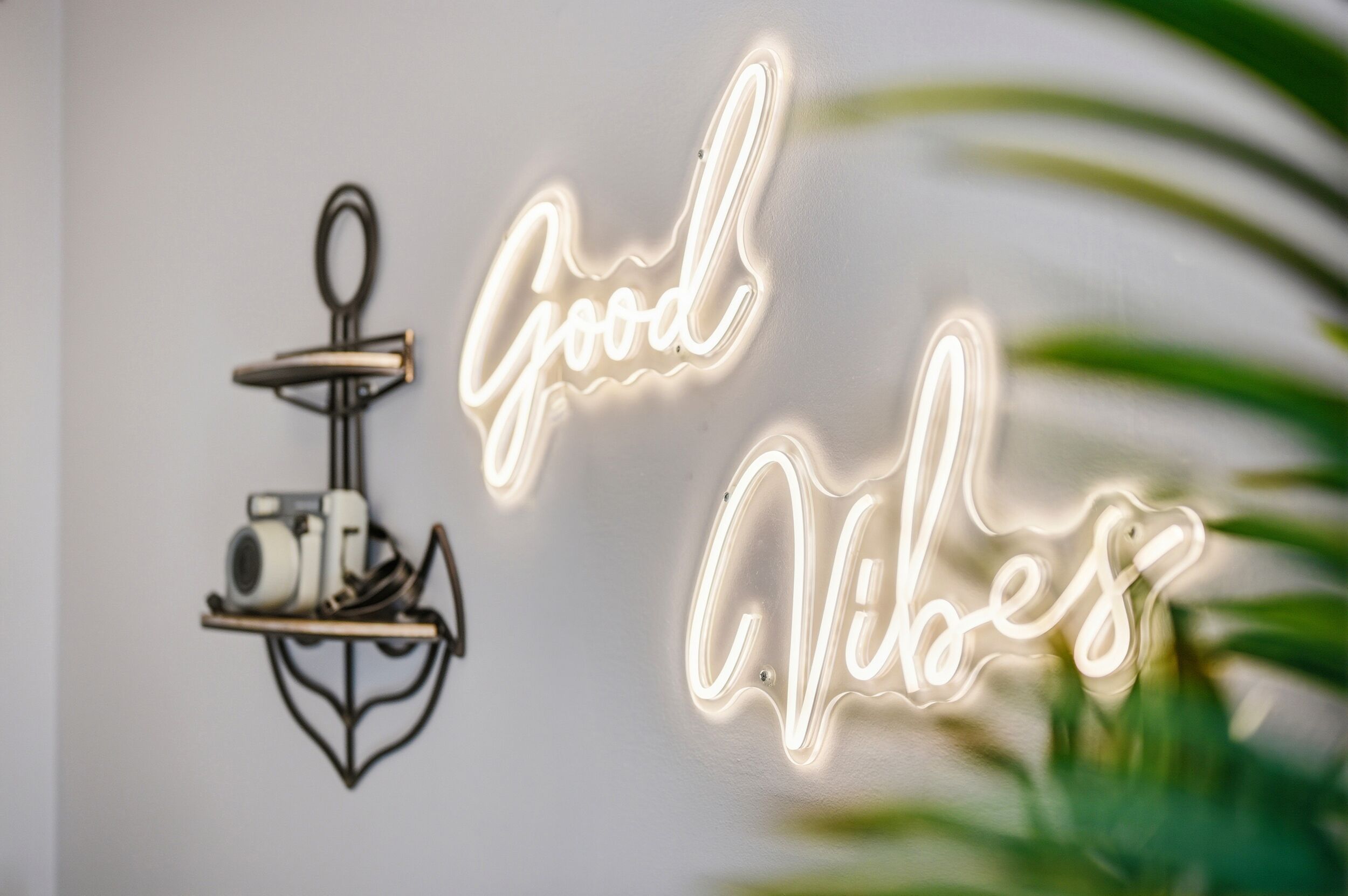 Un muro con un neon che recita 'Good Vibes' e una fotocamera su uno scaffale.