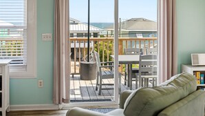 A living room with a view of a wooden deck and ocean.