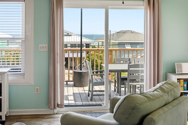 A living room with a view of a wooden deck and ocean.