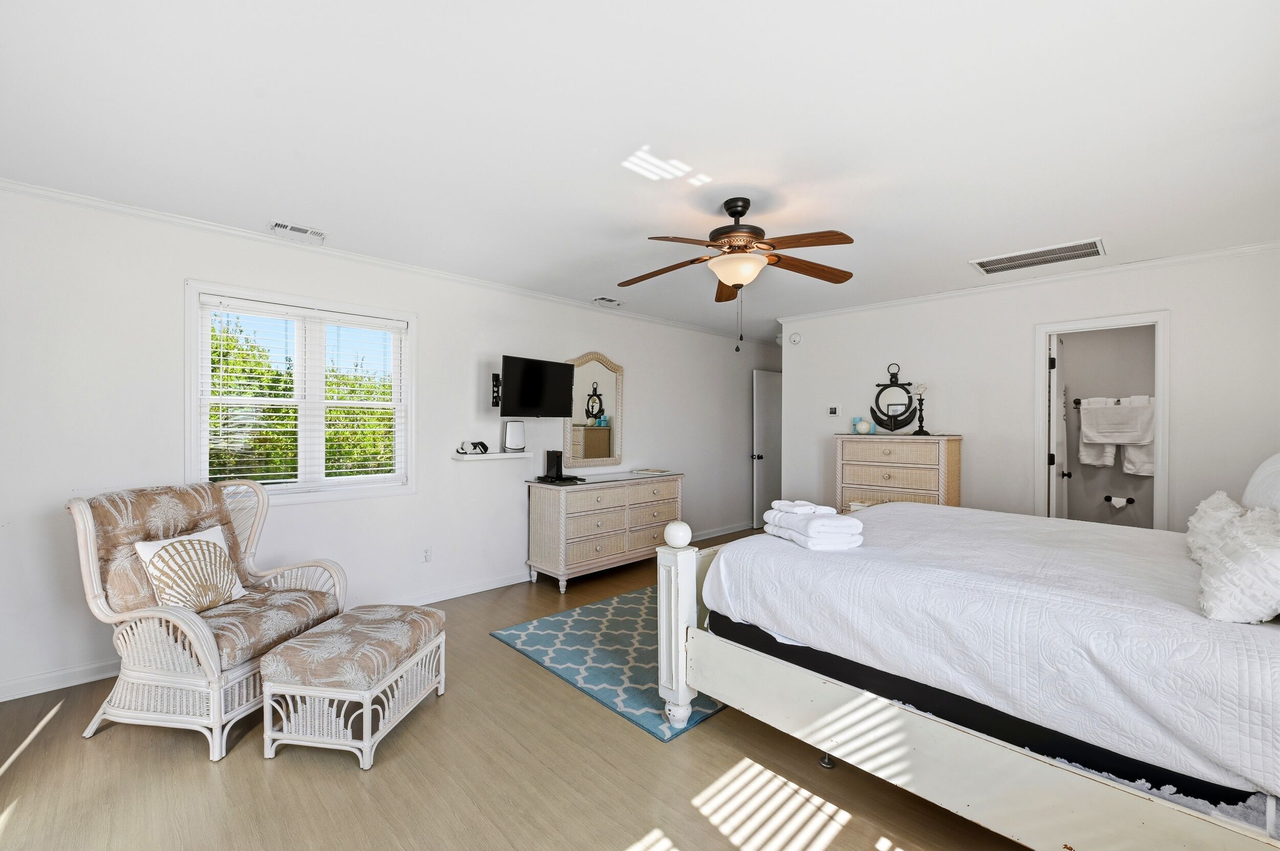 A bedroom with a bed, a chair, a dresser, a mirror, a ceiling fan, and a window.