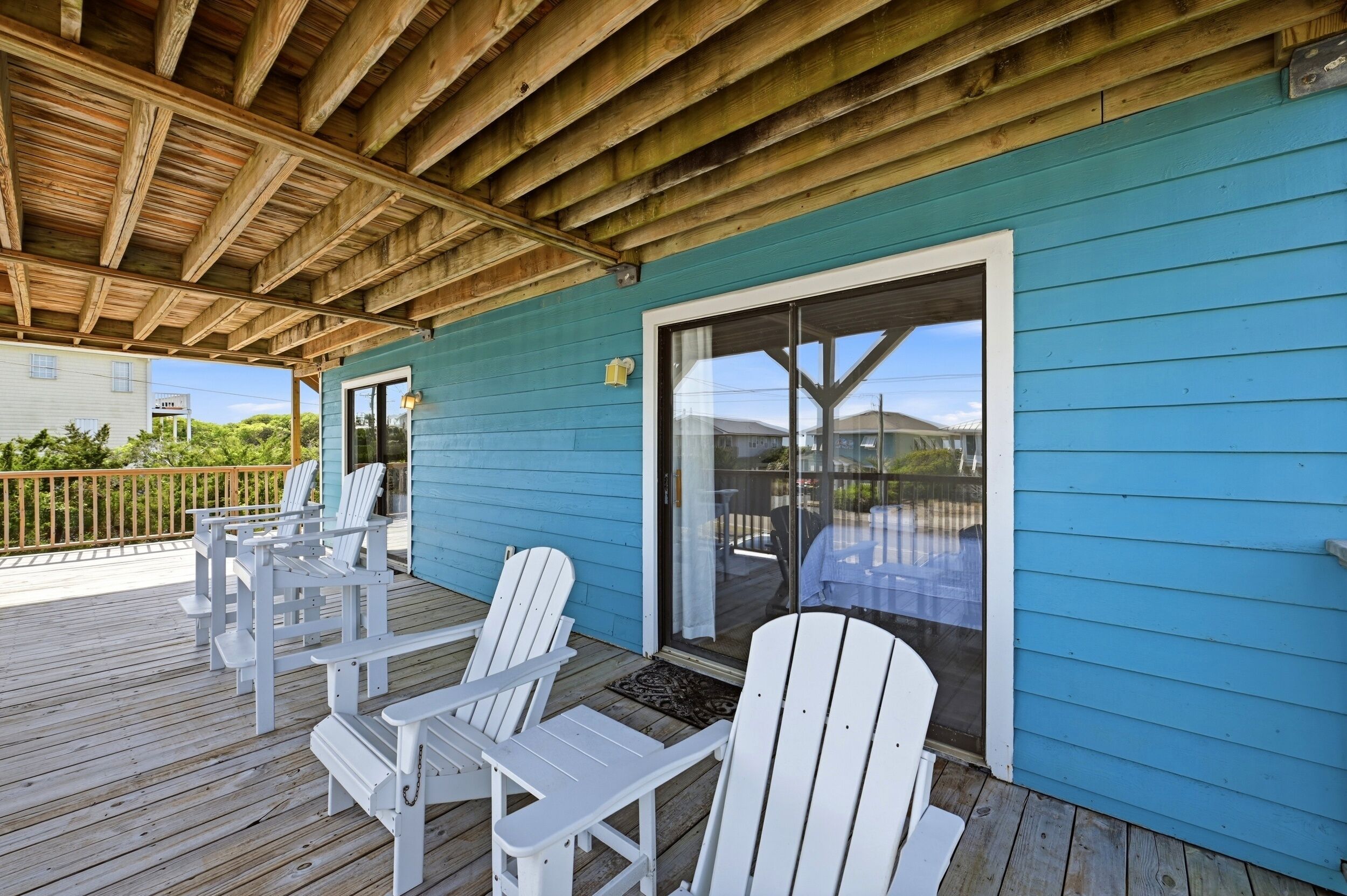 A covered deck with white Adirondack chairs, a glass door, and a blue exterior wall.