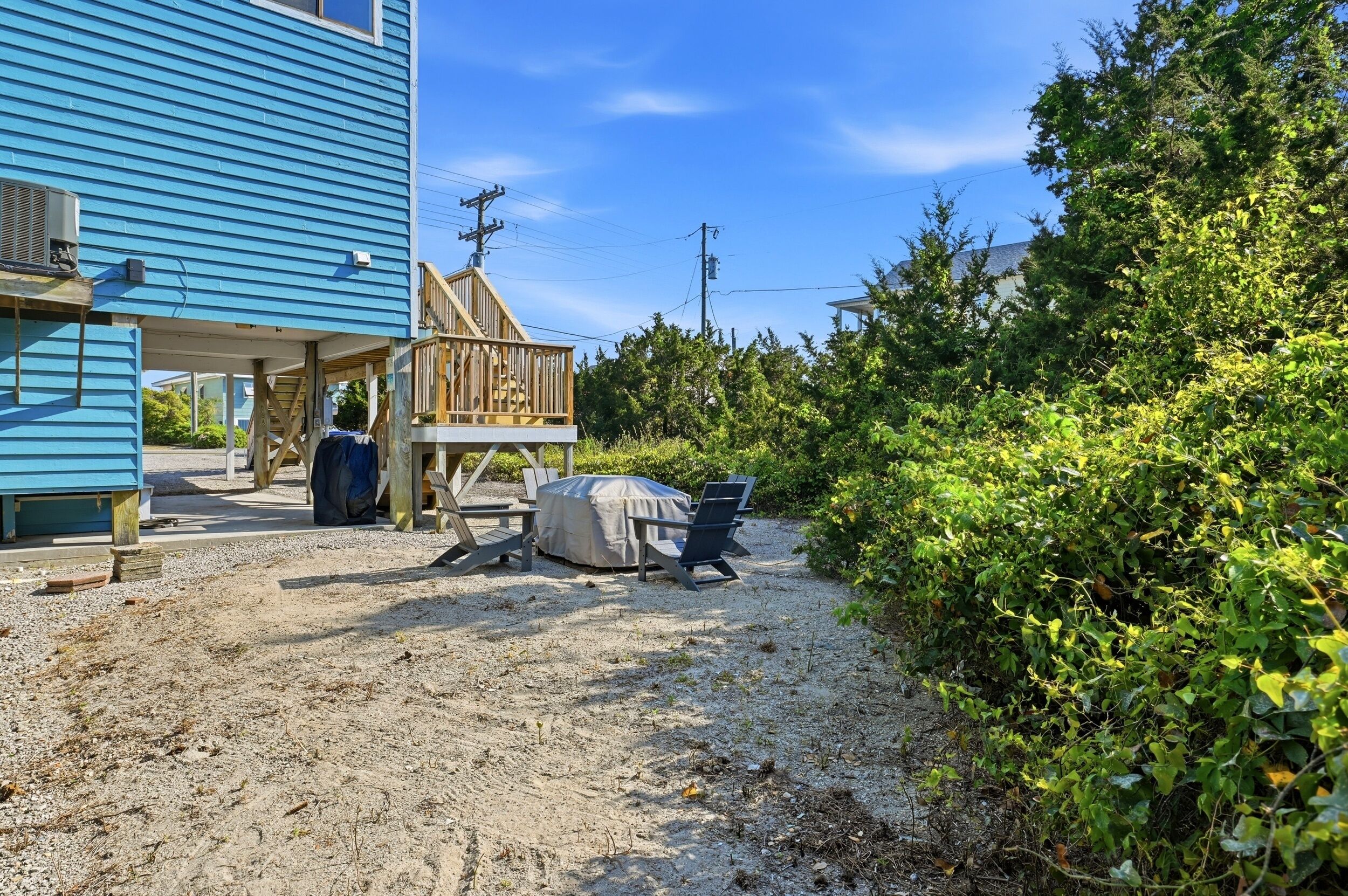 A house with a covered outdoor seating area, a wooden deck, and a gravel driveway.