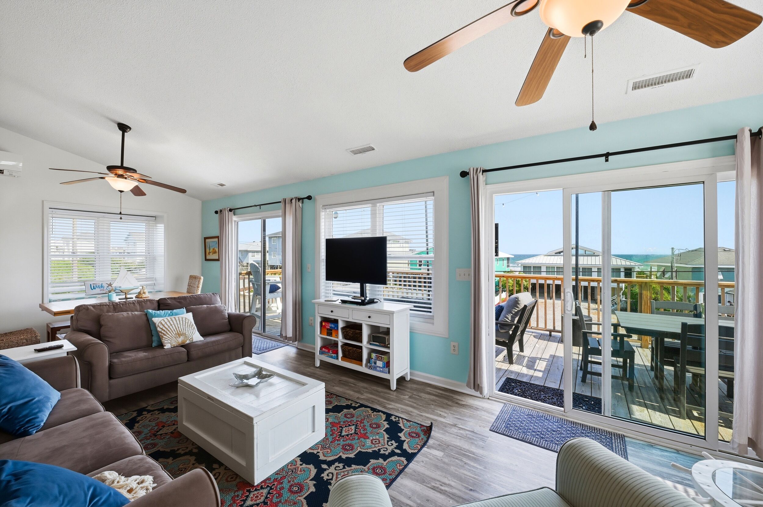 Un salon spacieux doté d’un ventilateur de plafond, d’un téléviseur à écran plat et d’un balcon aménagé avec du mobilier d’extérieur.