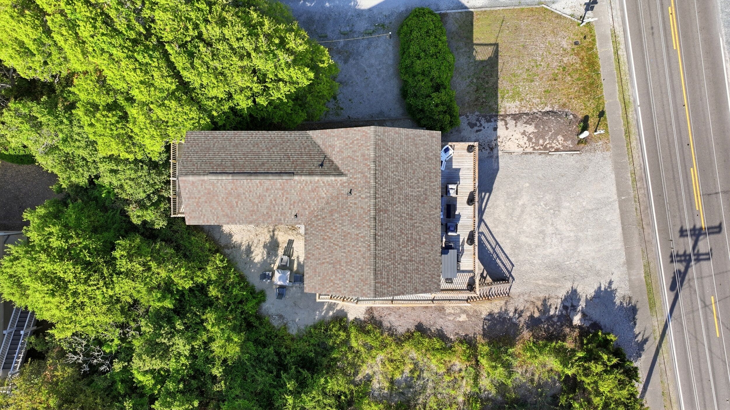 An aerial view of a building with a tiled roof, surrounded by trees and a paved area with a dock.