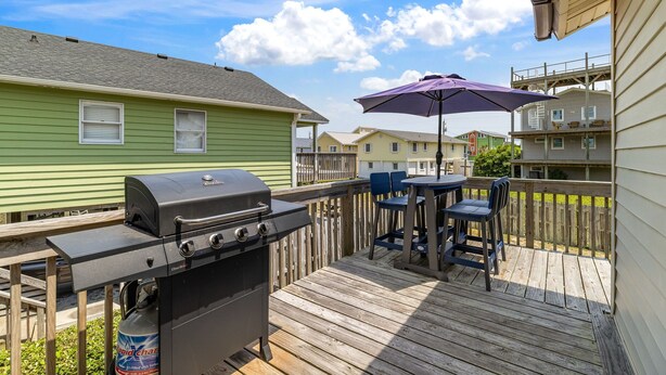A deck with a grill, outdoor table, chairs, and a purple umbrella.