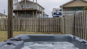 Een jacuzzi in een achtertuin met een houten omheining en huizen op de achtergrond.