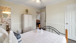 Een slaapkamer met een bed, een plafondventilator, een kledingkast en een zichtbare badkamer door een open deur.