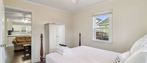A bedroom with a large bed, a ceiling fan, a window with a view, and a door leading to a bathroom.