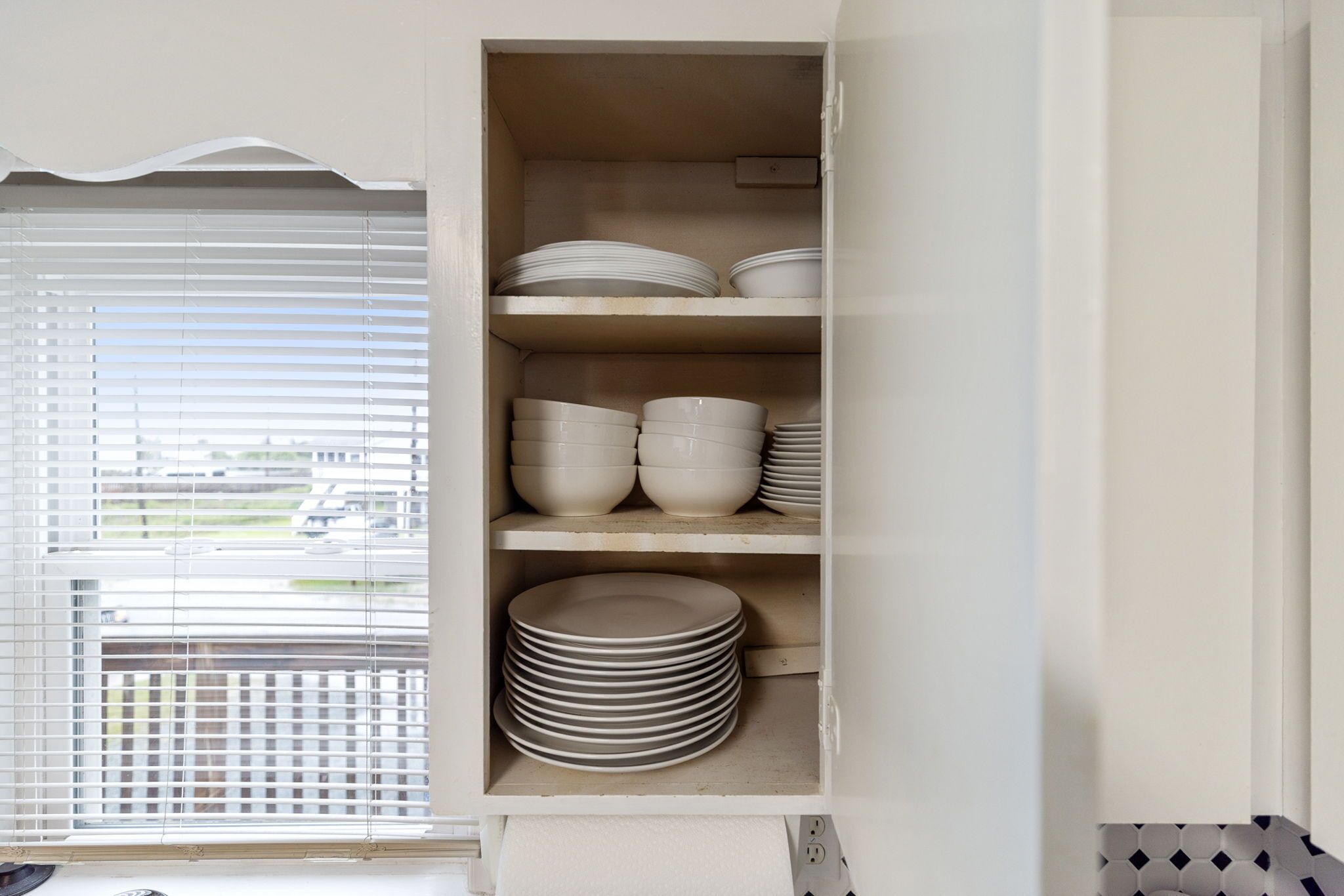 A white cabinet with shelves holding plates and bowls.