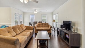 A living room with a sofa, a coffee table, a TV on a stand, and a ceiling fan.