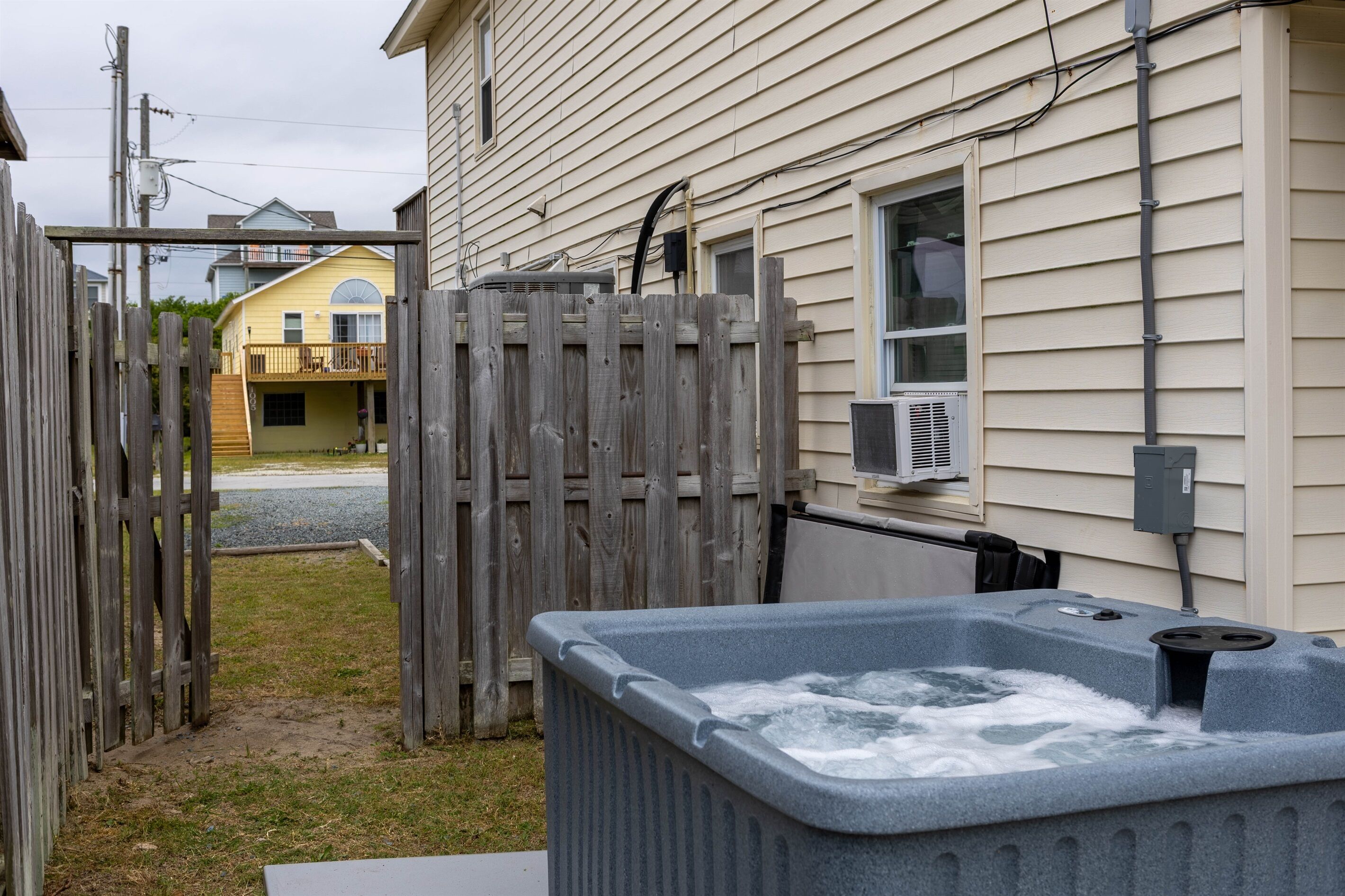 Un jardin avec un jacuzzi, une clôture en bois et une maison dont le revêtement extérieur est de couleur beige.